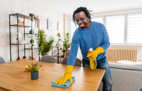 Handsome young black man wiping the dining table in his apartment.